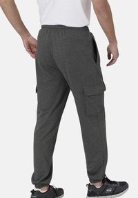 Graue Fleece-Jogginghosen mit einem elastischen Bund, Seitentaschen und einer Cargo-Tasche am rechten Bein. Die Bündchen sind an den Knöcheln angepasst.