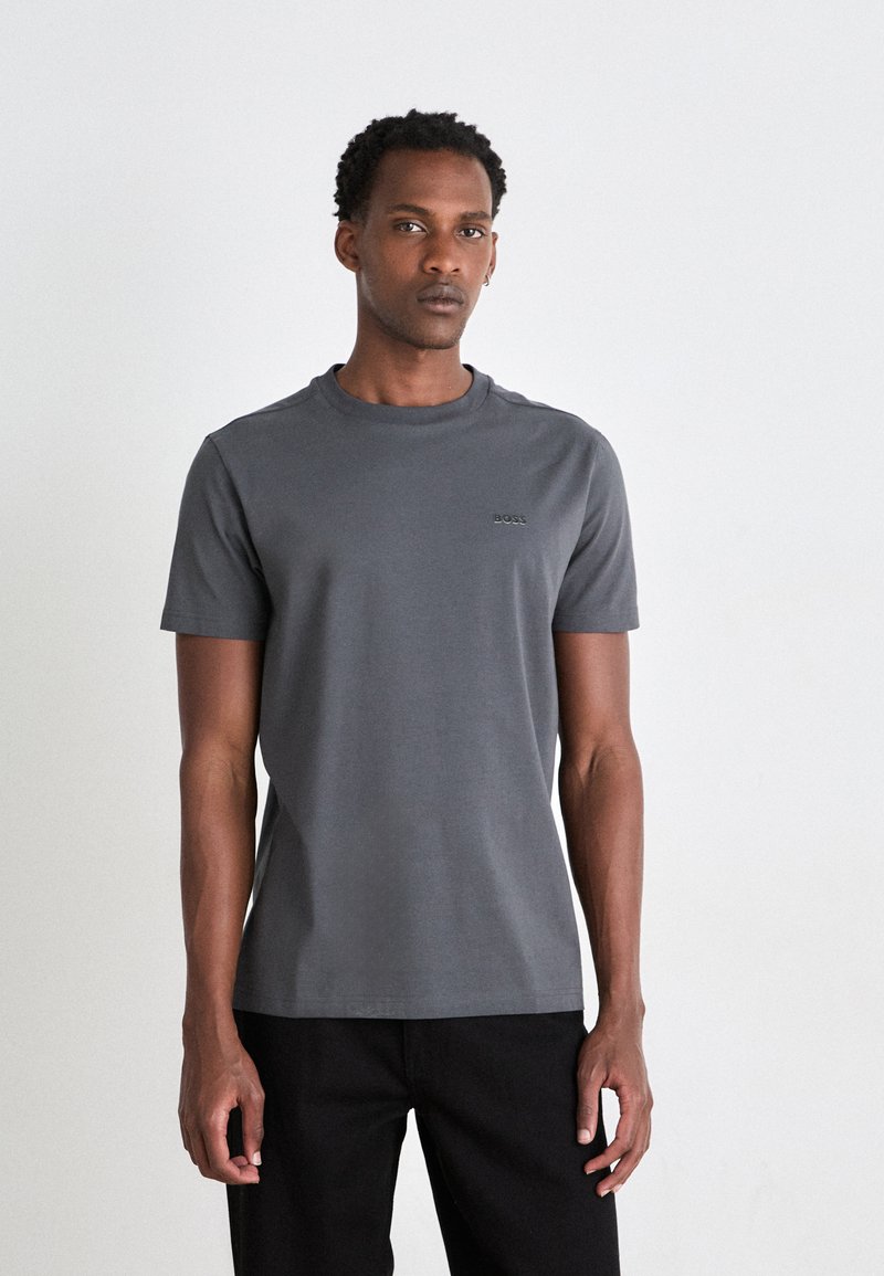 Grå kortærmet t-shirt lavet af bomuld, med rund hals og et diskret "BOSS" logo på brystet, parret med mørke bukser.
