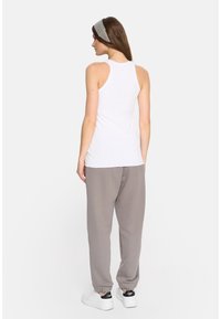 Biała, bezrękawnikowa koszulka na ramiączkach, wykonana z miękkiej tkaniny, o dopasowanym kroju. Do tego luźne, szare spodnie dresowe typu jogger i białe trampki.