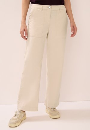 Pantaloni cargo beige a gamba larga con tasche frontali, chiusura con bottone e passanti per cintura, realizzati in un tessuto leggero. Abbinati a sneakers beige.