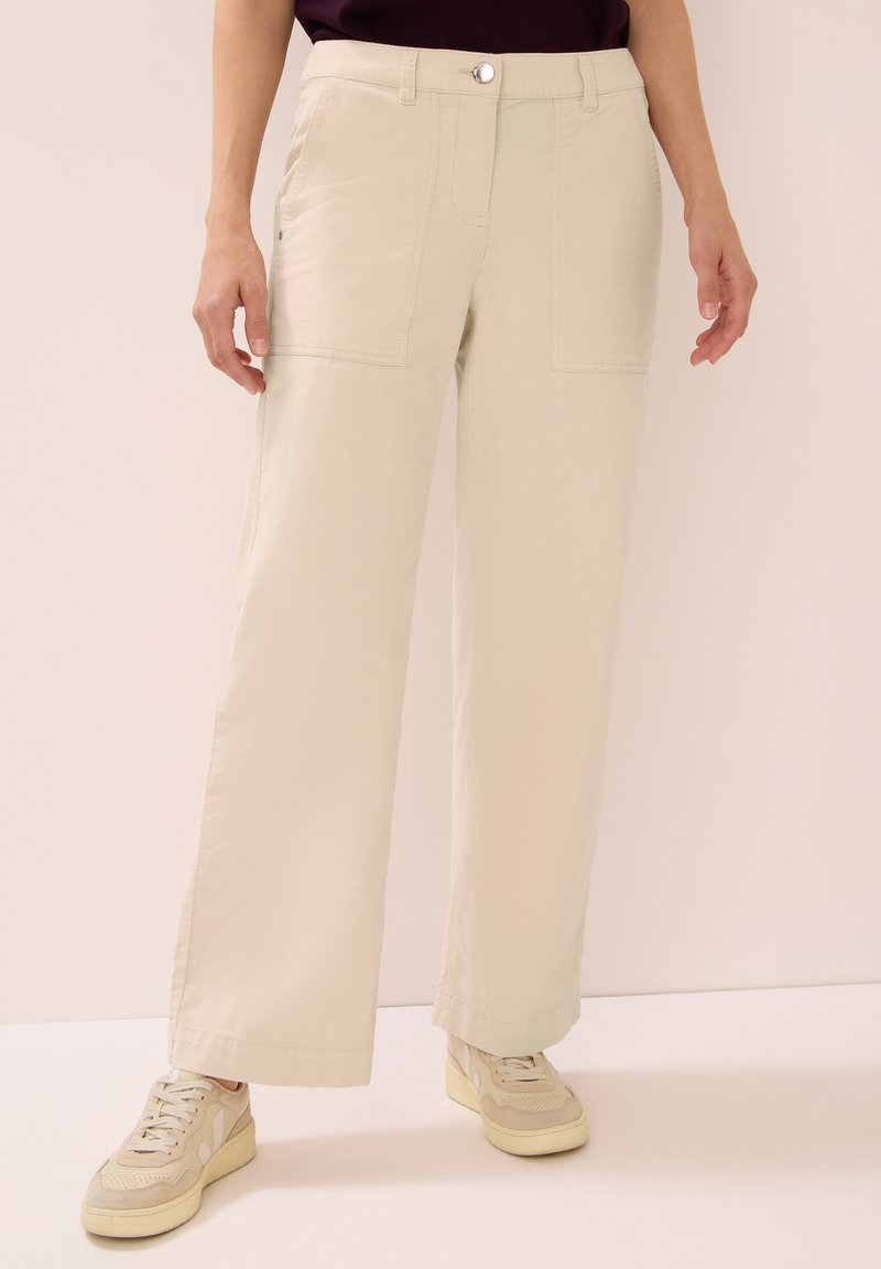Béžové široké cargo kalhoty s předními kapsami, zapínáním na knoflík a poutky na pásek, vyrobené z lehkého materiálu. S kombinací béžových tenisek.