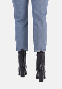 Bottines en cuir noir avec un talon épais, dotées de fermetures éclair latérales et d'accents de couture verticale. Portées avec un jean droit bleu clair.