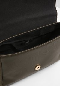 Olivgrüne Ledertasche mit einem strukturierten Design. Verfügt über einen goldfarbenen, runden Druckknopfverschluss und ein glattes schwarzes Innenfutter.