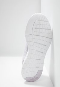 Baskets blanches avec une semelle en caoutchouc texturée, présentant un motif en grille. Les matériaux comprennent du mesh avec des accents lavande subtils et un détail de marque.