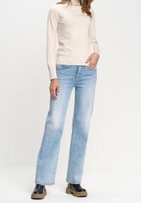 Beige rolák, světle modré široké džínové kalhoty a černé platformové kotníkové boty. Hladké pletení, vybledlý denim a design s robustní podrážkou.