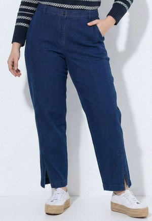 Personne portant un pantalon droit bleu foncé avec des poches avant, des fentes sur les côtés à l'ourlet, des baskets blanches à plateforme et un pull rayé.