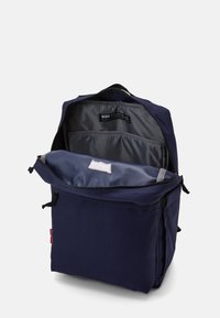 Navy blue backpack with a spacious, gray-lined interior, featuring a zip closure, front pocket, and fabric logo patch inside.
