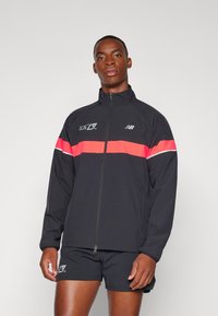 Black zip-up jacket featuring a prominent pink horizontal stripe, logo detailing, and a lightweight design. Short black shorts complete the outfit.