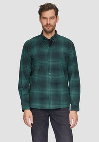 Groene geruite overhemdbloes met een ruitpatroon, lange mouwen en zwarte knopen, gecombineerd met donkere jeans. Gelaagd stof.