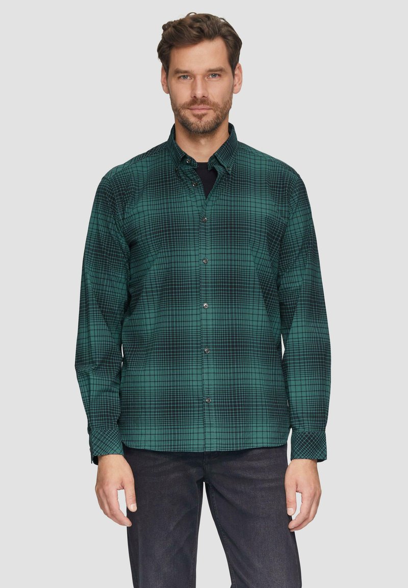Groene geruite overhemdbloes met een ruitpatroon, lange mouwen en zwarte knopen, gecombineerd met donkere jeans. Gelaagd stof.