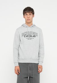 Sudadera gris con cordón, con un logo impreso "JACK & JONES Coll. Studio." Textura suave y puños y dobladillo acanalados.