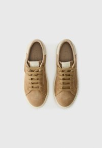 Une paire de baskets en suède beige avec des semelles et des lacets beiges, vue de dessus sur un fond blanc.