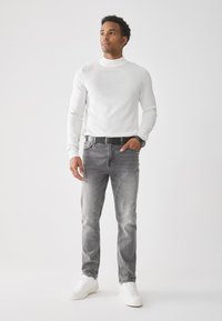 Suéter blanco de cuello alto, jeans gris ajustados y zapatillas blancas. Presenta un cinturón negro, diseño sencillo y un ligero desgaste en los jeans.