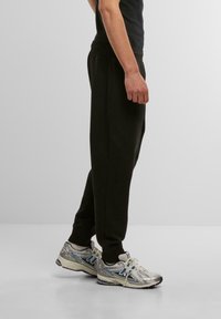 Svarta träningsbyxor med elastiskt midjeband, tapered ben och subtil textur. Kombinerat med grå och blå löparskor med en reflekterande design.