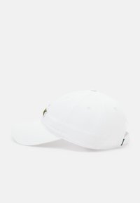 Boné de beisebol branco feito de algodão, com uma aba curva, detalhes bordados em verde e vermelho na frente, e uma faixa ajustável na parte de trás.