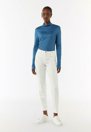 Blaues Langarmoberteil mit Stehkragen, kombiniert mit weißen Slim-Fit-Hosen und weißen Sneakern. Glatte Textur und minimalistisches Design.