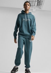 Set di felpa e joggers color teal con cappuccio, caratterizzato da un logo bianco "Sportswear by PUMA". Tessuto morbido, vestibilità comoda, polsini elasticizzati.