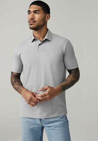 Graues Poloshirt mit kurzen Ärmeln und Kragen, ausgestattet mit einer Drei-Knopf-Leiste und einem kleinen gestickten Logo auf der Brust.