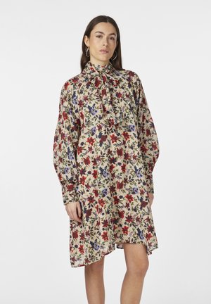 Floral dress in beige, featuring a bow tie collar, long sleeves, and varied flower patterns in red, blue, and green on soft fabric.