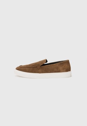 Pantofi slip-on din suede maro, cu talpă din cauciuc albă și detalii de cusătură subtile, având vârful rotunjit și fără dantelă vizibilă.