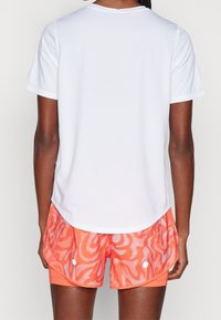 Biała sportowa koszulka z krótkim rękawem i okrągłym dekoltem, zestawiona z pomarańczowymi szortami w wzory z białymi akcentami i teksturą przypominającą siateczkę.