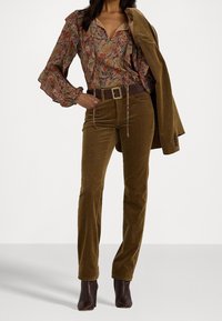 Färgglad blus med blomstertryck och volangärmar, bruna kordflamsbyxor och ett matchande bälte; bruna klackade ankelstövlar.