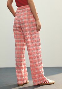 Lätta, rosa rutig byxor med elastisk midja. Har en lös passform och raka ben, i kombination med vita träningsskor.