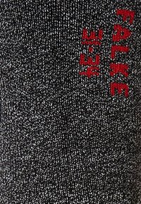 Tejido de punto gris con un patrón texturizado, con un audaz logotipo rojo "Falke" bordado en el lateral. El diseño es simple y moderno.