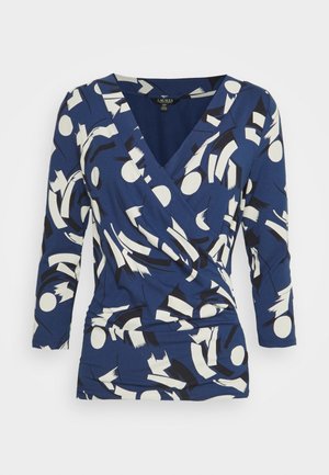 Navyblauwe wikkeltop van rekbaar materiaal met abstracte witte en zwarte patronen, met een v-hals en driekwartmouwen.