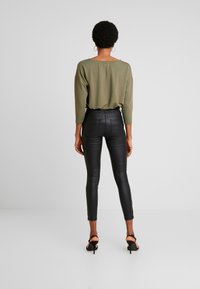 Top de manga larga verde oliva con hombros caídos combinado con pantalones ajustados de piel sintética negros de cintura alta y sandalias negras de tacón.