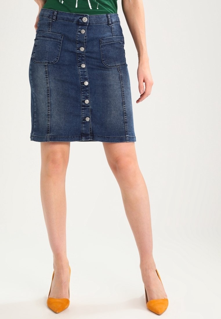 Farkkuhame, jossa on nappikiinnitys edessä, kaksi etutaskua, polven ylle ulottuva pituus, tumman värinen pesu ja istuva muotoilu. Yhdistetty keltaisiin korkokenkiin.