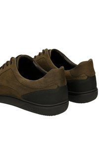 Hnědé semišové tenisky na zavazování s černým texturovaným gumovým podpatkem a podrážkou, zobrazené zezadu z úhlu tří čtvrtin.