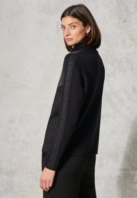 Pullover nero a maglia con colletto alto, caratterizzato da dettagli metallici lungo le maniche. Texture liscia con una vestibilità rilassata e apertura laterale.