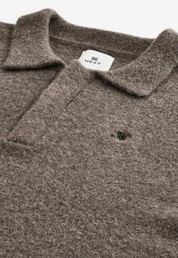 Braunes, filzartiges Polohemd mit strukturierter Oberfläche, ausgestattet mit einem klassischen Kragen und einem kleinen Logodetail in der Nähe der Brust. Markenlabel sichtbar.