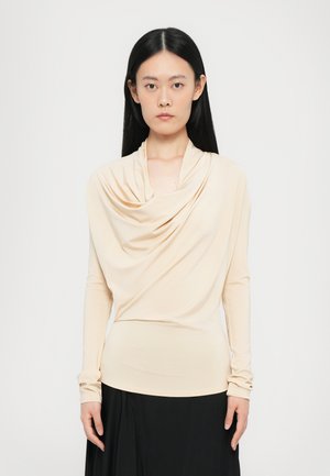 Beige lange mouwen top met een gedrapeerde colhals. Glad, rekbaar materiaal; strakke pasvorm benadrukt de vorm. Gecombineerd met een zwarte rok.