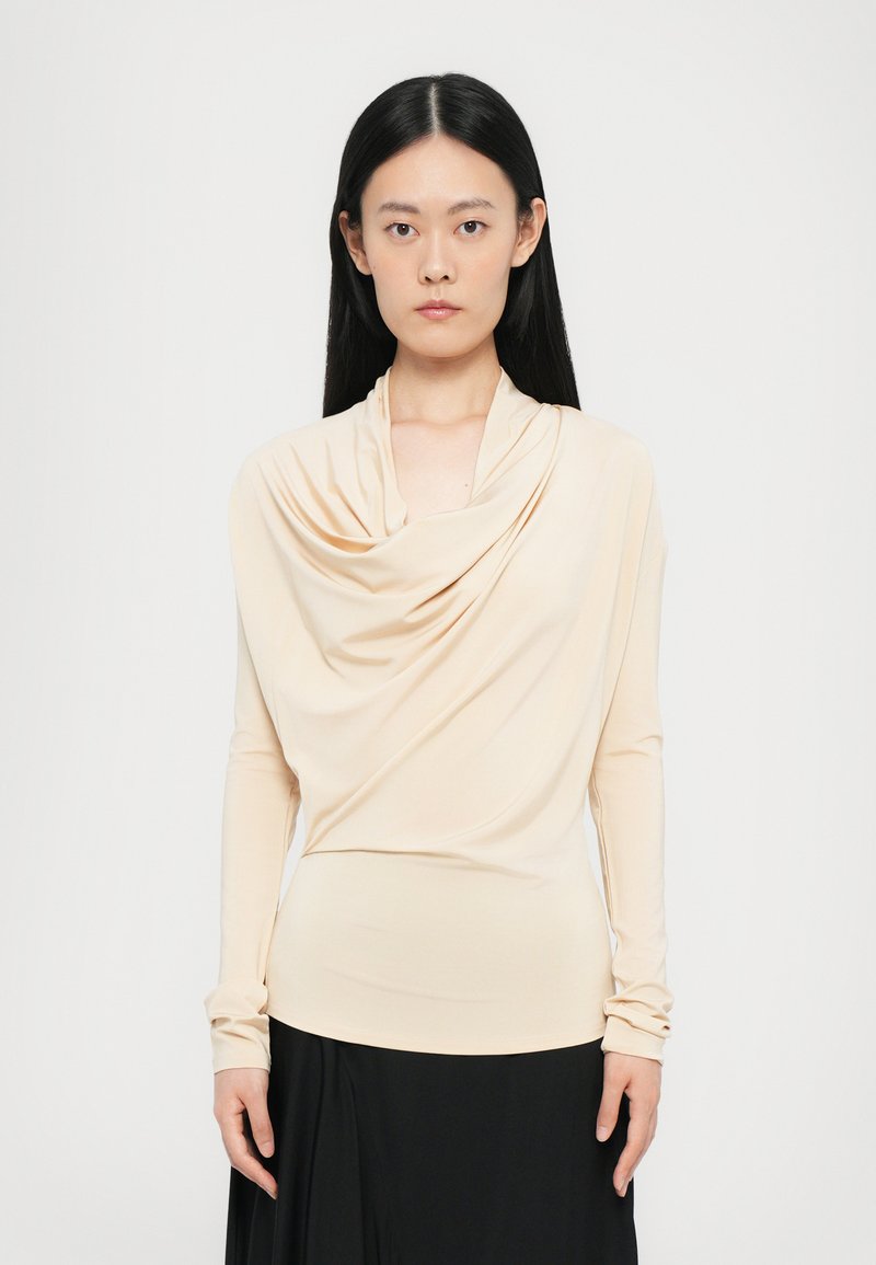 Beige lange mouwen top met een gedrapeerde colhals. Glad, rekbaar materiaal; strakke pasvorm benadrukt de vorm. Gecombineerd met een zwarte rok.