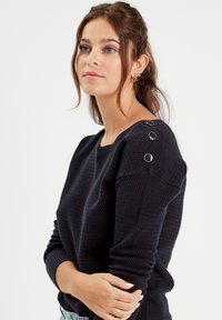 Navy blue textured sweater with boat neckline, feature buttons on shoulder, long sleeves, and a relaxed fit.