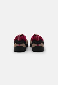 Chaussures avec une tige en suede beige et en mesh, accentuées de détails noirs et de rayures rouges. Semelle plate en caoutchouc noir pour une bonne traction.
