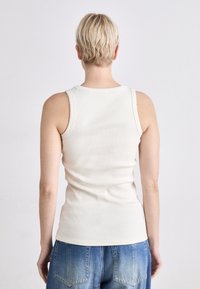 Witte geribde tanktop met een getailleerd ontwerp, ronde halslijn en brede schouderbanden, gecombineerd met blauwe denim broeken.