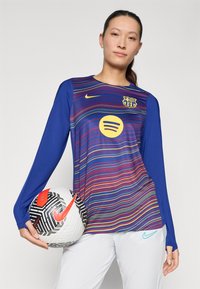 Nike'i pikka varrukaga Barcelona jersei sinises värvitoonis, millel on mitmevärvilised laine mustrid, sisaldab ümmargust Spotify logo ja klubilogo. Must-valge jalgpall on hoitud.