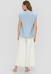 Blauw-wit gestreepte blouse met korte mouwen en een gebogen zoom, gecombineerd met witte wijde broek en beige sandalen.