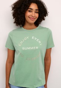 Groene katoenen t-shirt met korte mouwen met een cirkelvormig tekstontwerp in metallic goud: "Geniet van elk moment van de zomer."