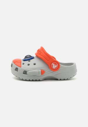Sabot gris clair avec bride de talon orange, embout orange, et décoration oculaire bleue sur le dessus, doté de trous de ventilation et d'une semelle texturée.