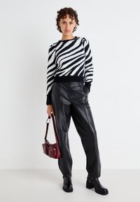 Maglione peloso a righe bianche e nere, pantaloni in pelle neri a vita alta, stivali neri fino alla caviglia e una piccola borsa bordeaux.