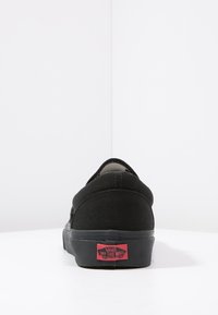 Black canvas sneaker with a low-cut design, rubber sole, and prominent red logo stitched on the heel. Smooth texture and minimal detailing.