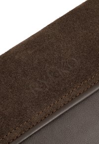 Cartera de ante y cuero marrón con el nombre de la marca "RYKKO" en relieve y costuras en contraste a lo largo del borde. Textura suave con acabado mate.