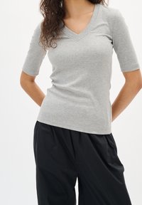 Grå ribbad kortärmad topp med v-ringning och figurnära passform, mjuk textur och diskreta sidospjäll, tillsammans med lösa svarta byxor.