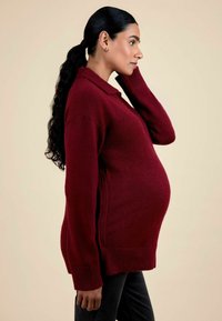 Pulover de maternitate din material plușat, de culoare burgundă, cu guler poli și manșete striate, prevăzut cu slituri laterale, conceput pentru confort și ușurință în timpul sarcinii.