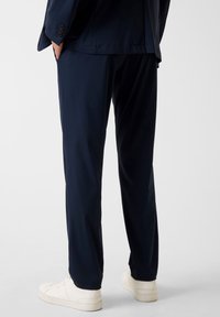 Marineblaue Hose mit glatter Textur, maßgeschneiderter Passform und seitlichen Taschen, kombiniert mit weißen Turnschuhen.