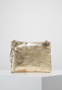 Złota torebka kopertowa o pogniecionej fakturze z gładkim metalicznym wykończeniem, zamek błyskawiczny oraz odczepiany łańcuszek, oferujący różne opcje noszenia.